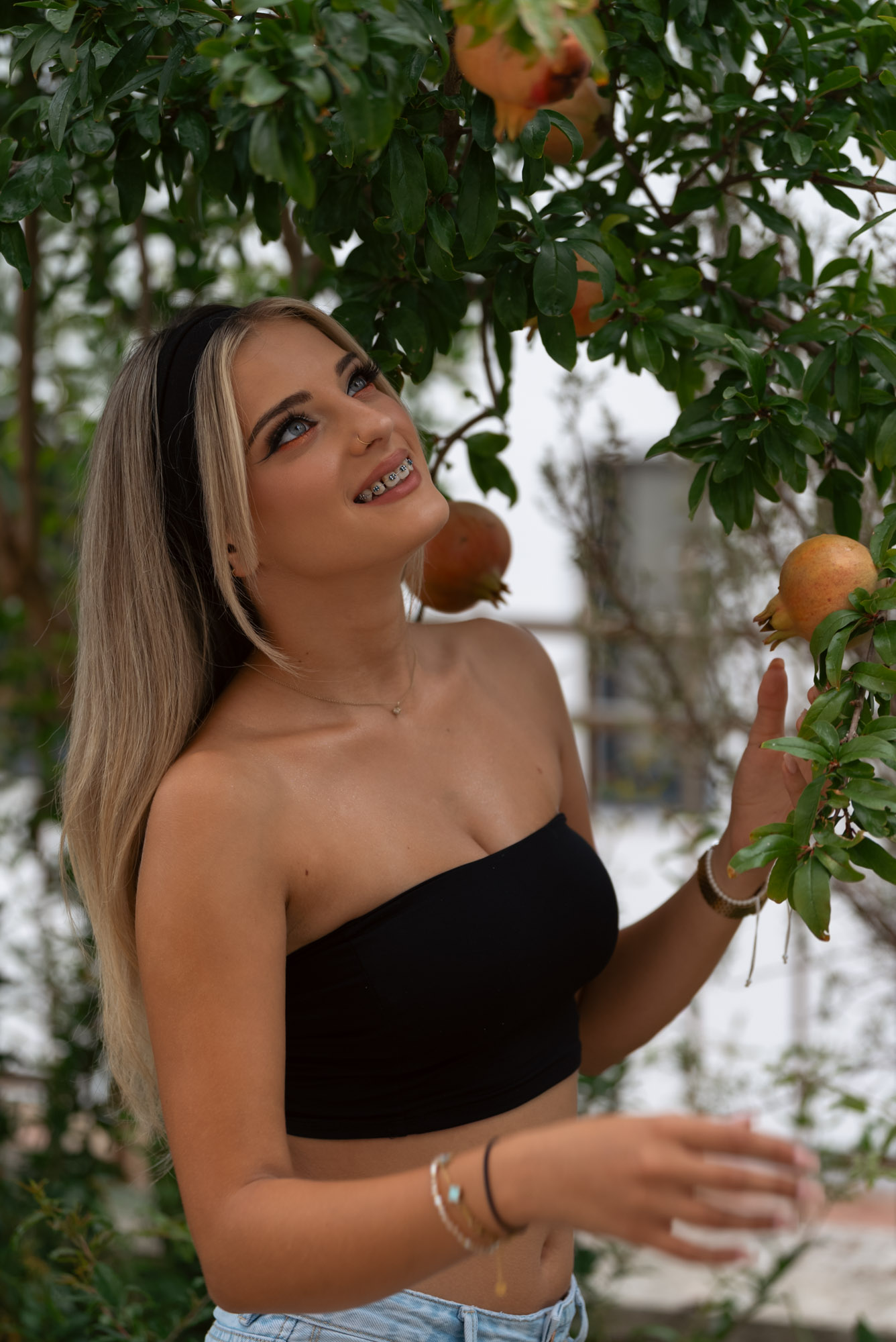 Smiling upward with a hand raised to the pomegranate branch