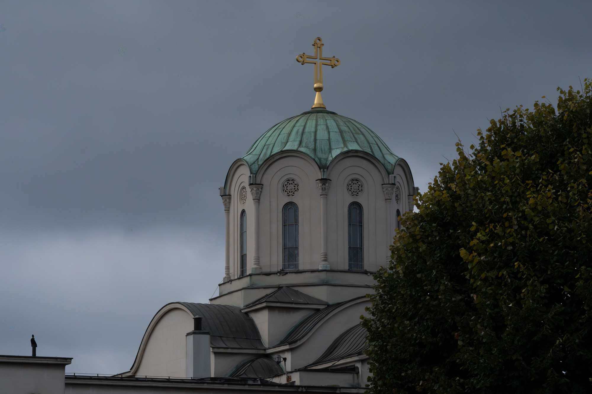 Orthodox church dome with green copper roof and gold cross against a stormy sky, Belgrade
