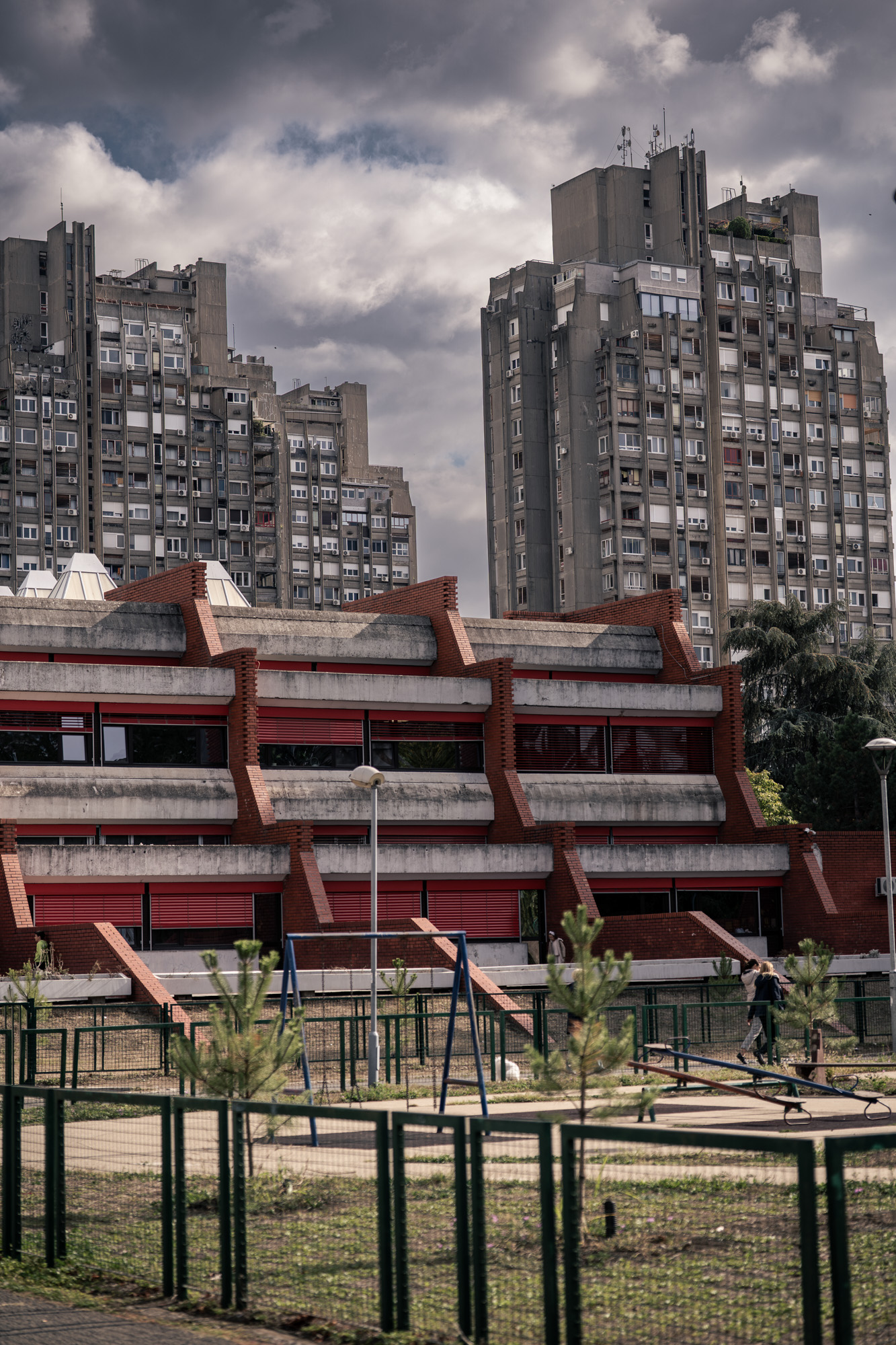 Novi Beograd — red-brick modernist building with concrete panel towers behind and playground in front